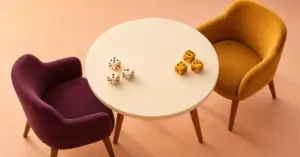 Vaalean pyöreän pöydän ääressä on kaksi vastakkaista tuolia ja pöydällä kaksi nopparyhmää kahden pelaajan peliä varten.