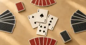 Tuppipelin neljää pelaajaa ja vastakkaisia pareja kuvaavat korttiviuhkat ympäröivät neljästä patakortista muodostuvaa tikkiä vaalealla pöydällä.